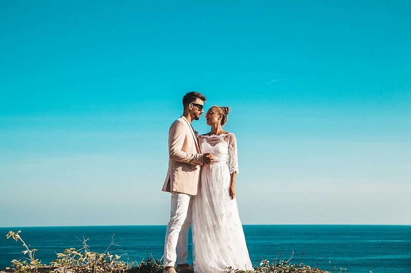 Portrait of bride and groom posing on the cliff behind blue sky and sea. Wedding Couple
